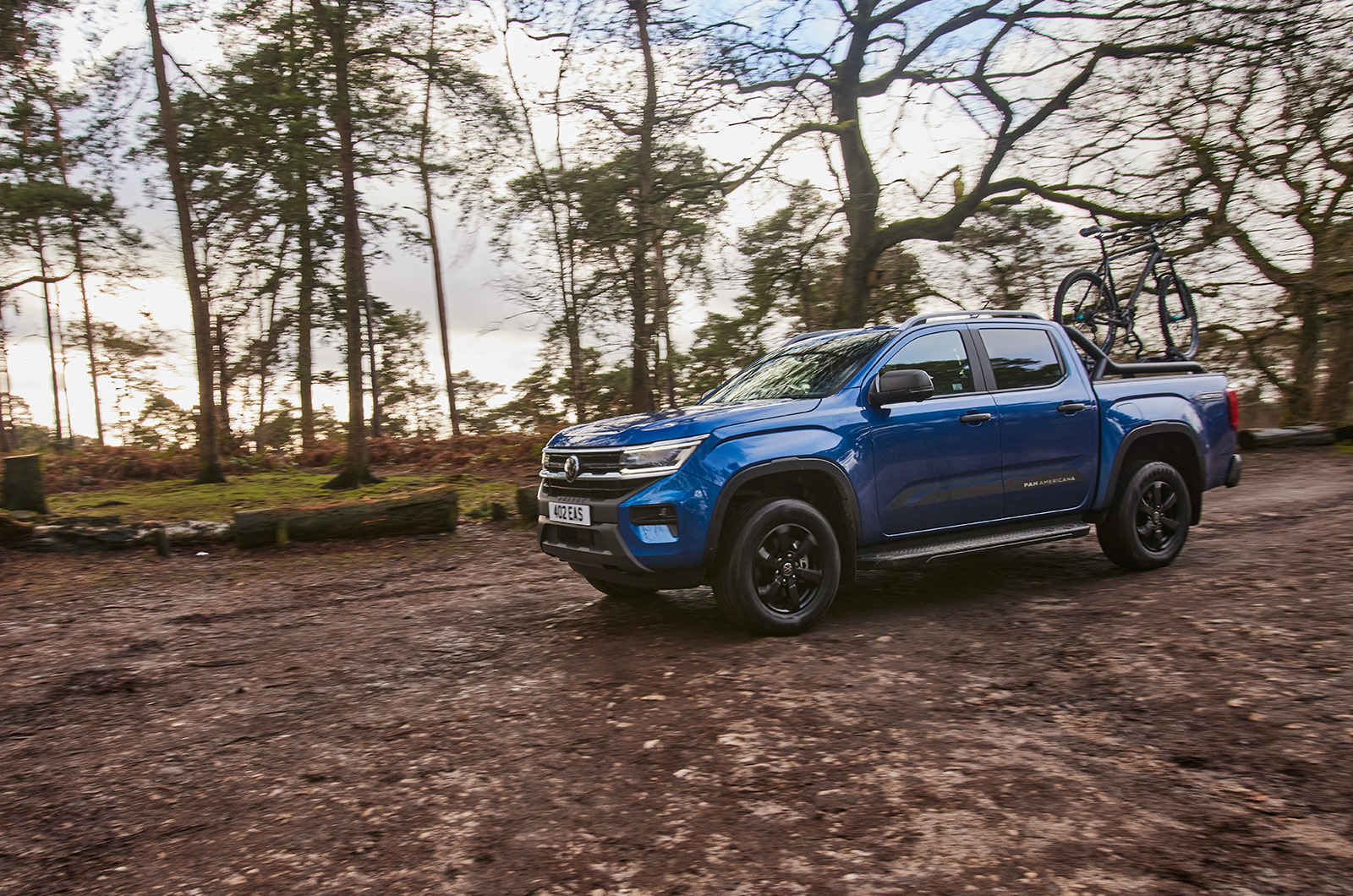A blue Volkswagen Amarok pick-up drives on muddy terrain