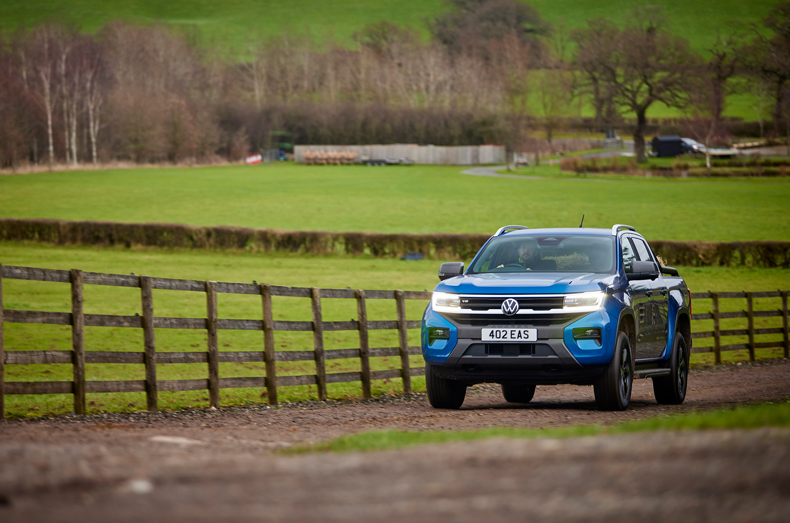 A blue Volkswagen Amarok pick-up drives down a rural dirt track