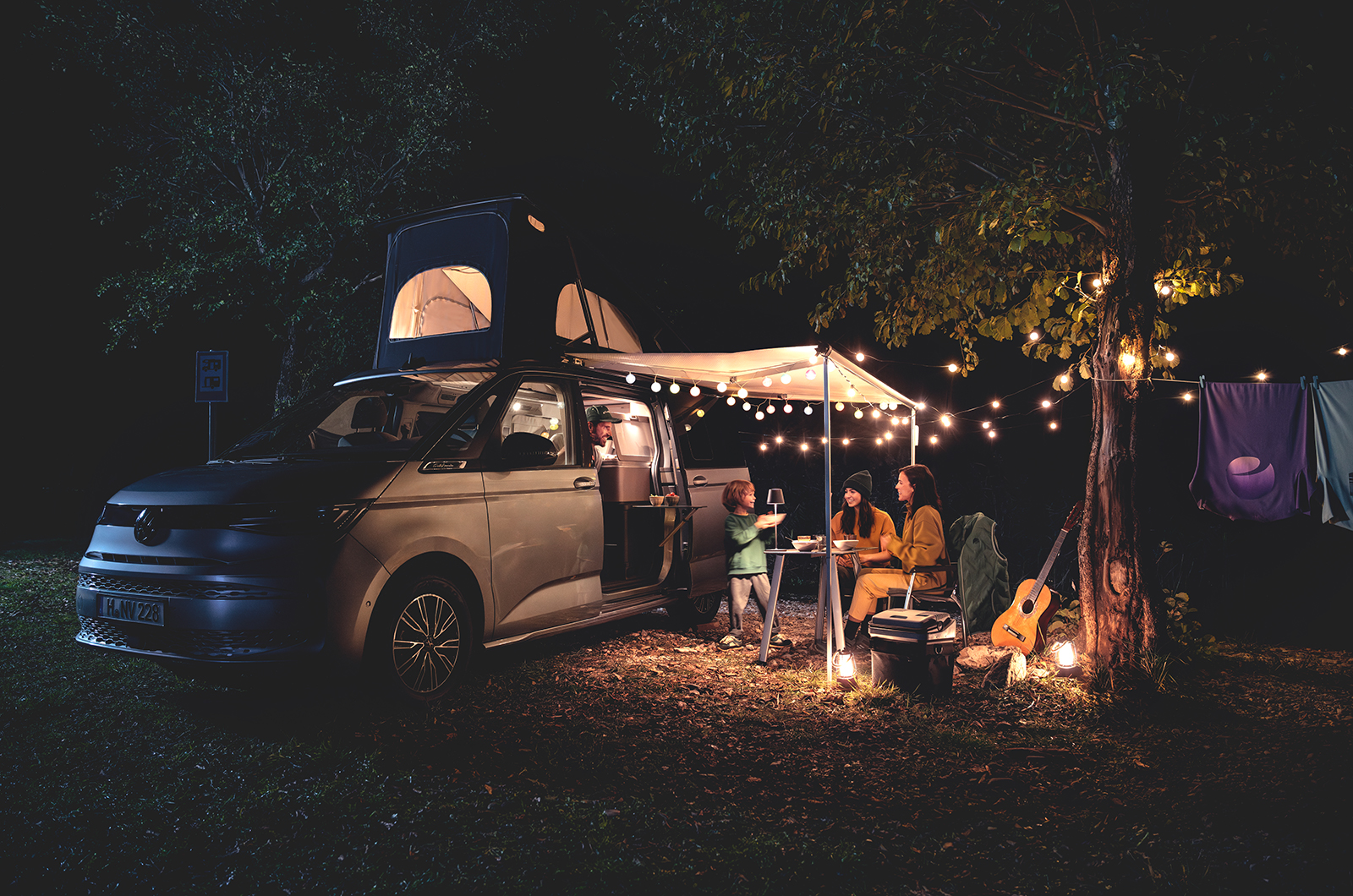 Volkswagen California with family sat under awning at night