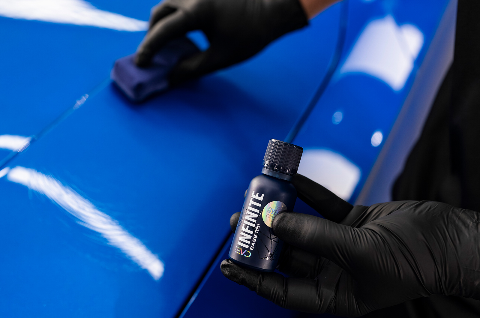 A Gyeon technician applies Infinite ceramic coating to a blue car 