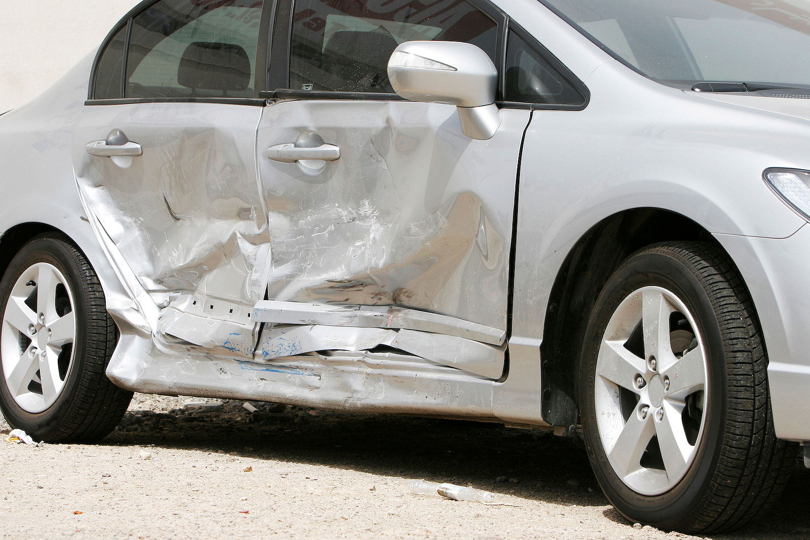 A silver coloured car with crash damage to the doors