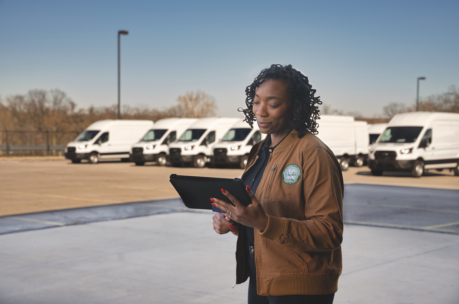 Woman looks at tablet with Ford vans in the background