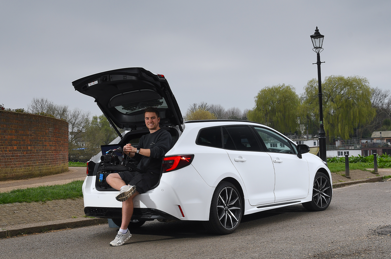Jonty sitting in LT Toyota Corolla Touring Sports boot and holding a camera