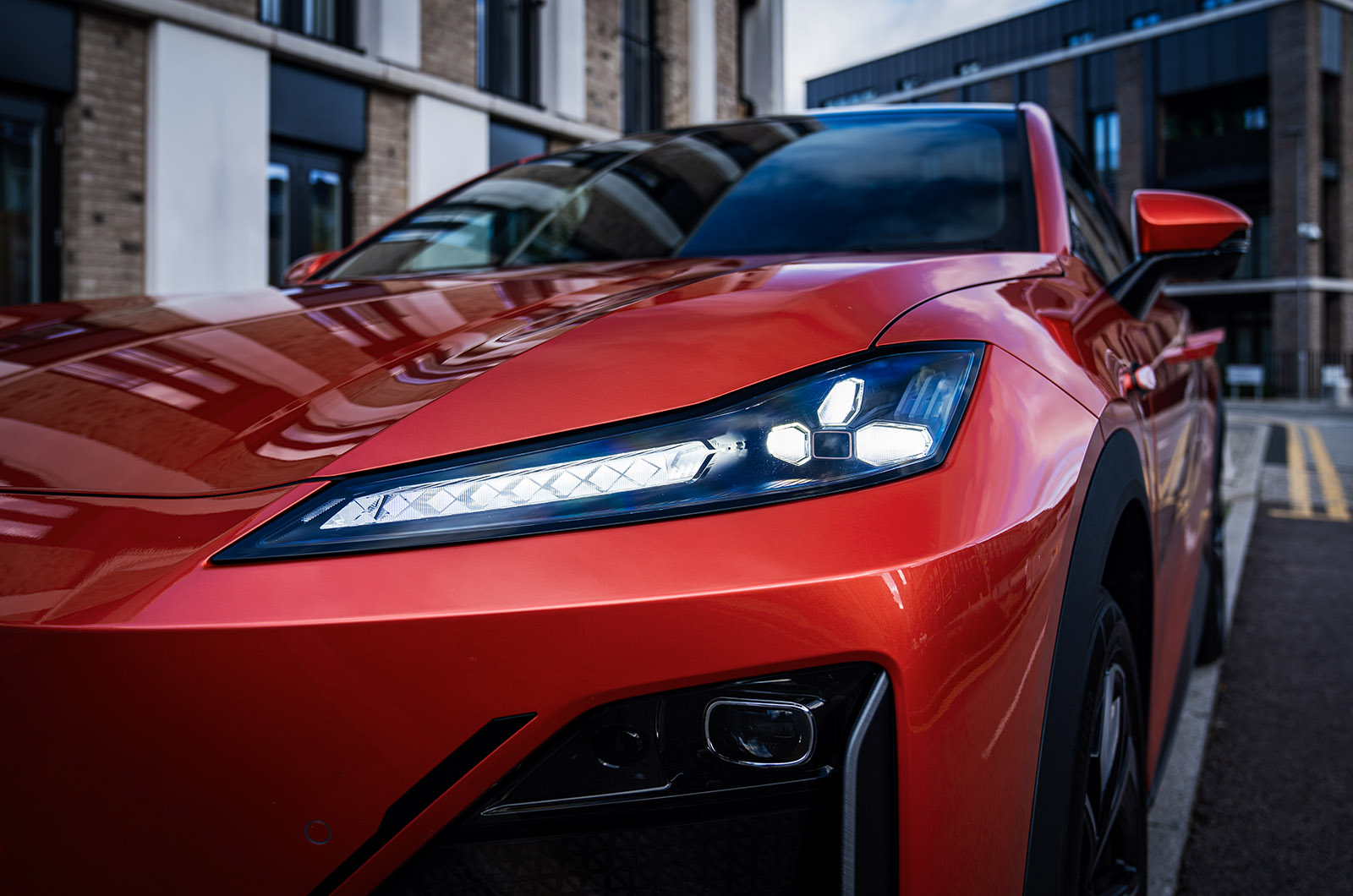 A detail shot of an LED headlight on an orange Changan Deepal S07 parked in a modern residential area