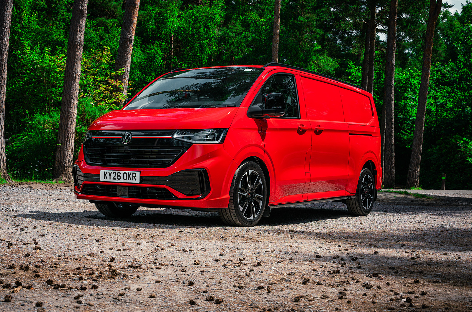 A red Volkswagen Transporter Sportline parked in a woodland area viewed from the front three-quarter