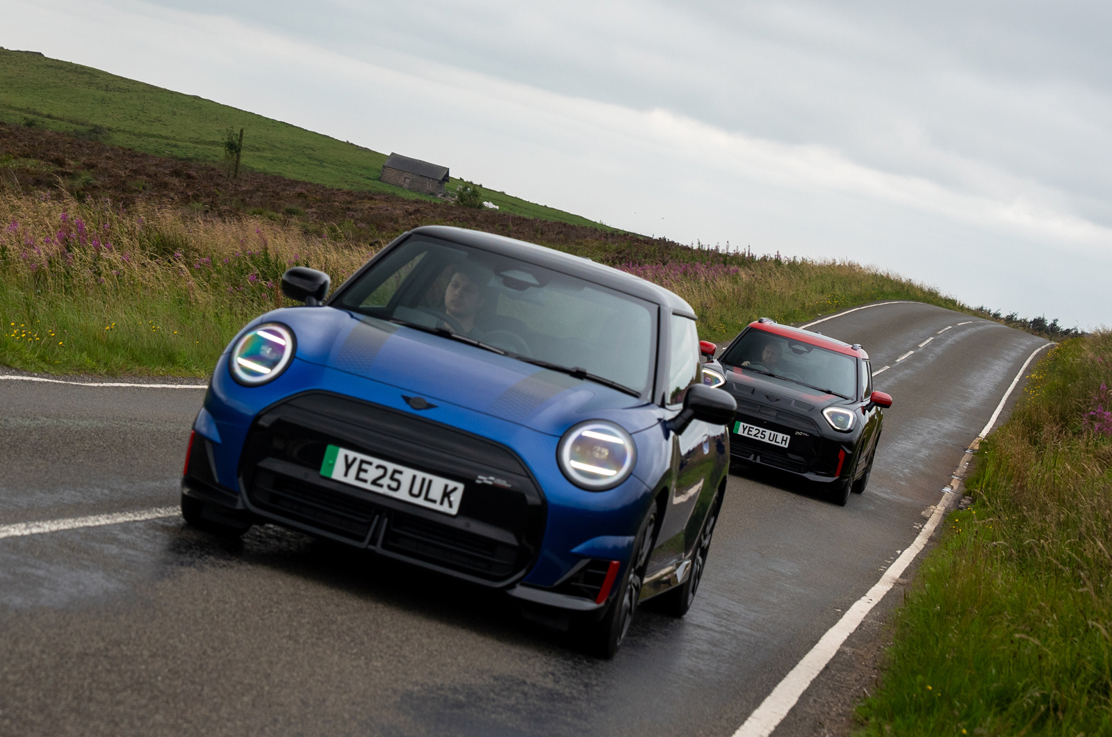 A blue MINI JCW Electric driving ahead of a black and red MINI John Cooper Works Aceman