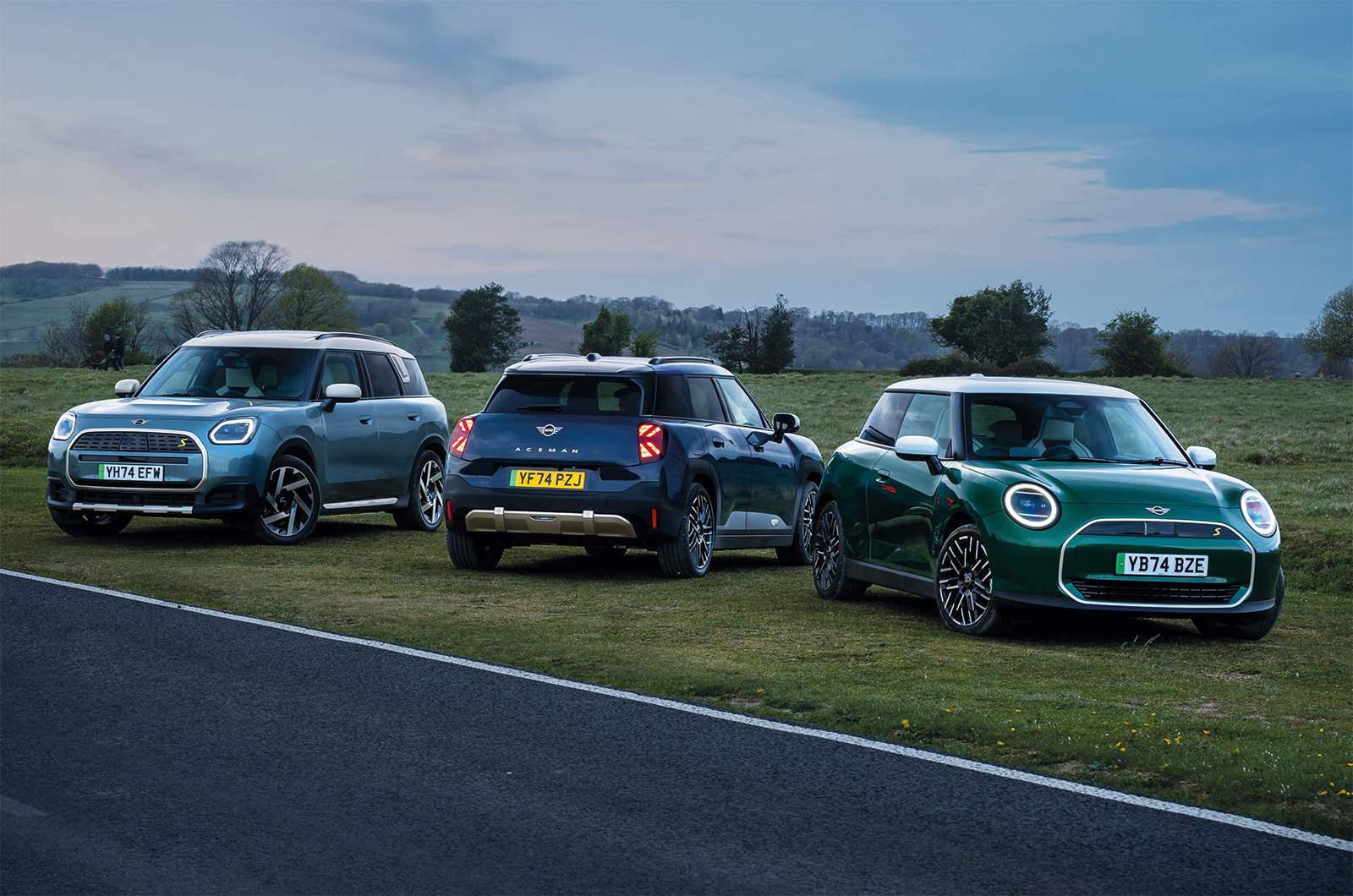 The all-electric Cooper, Aceman and Countryman parked together in front of a scenic countryside backdrop