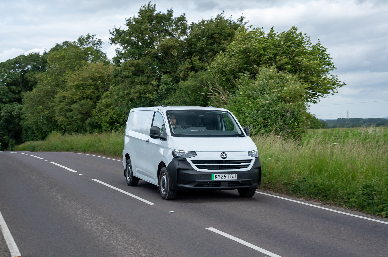 A white Volkswagen Transporter driving down a country road viewed from the front three-quarters