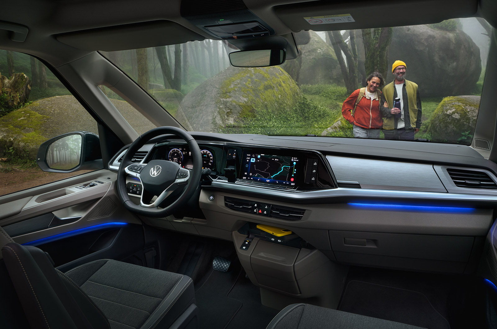 Interior shot of the Volkswagen California showing the front dash area and two passengers standing in front of the camper van