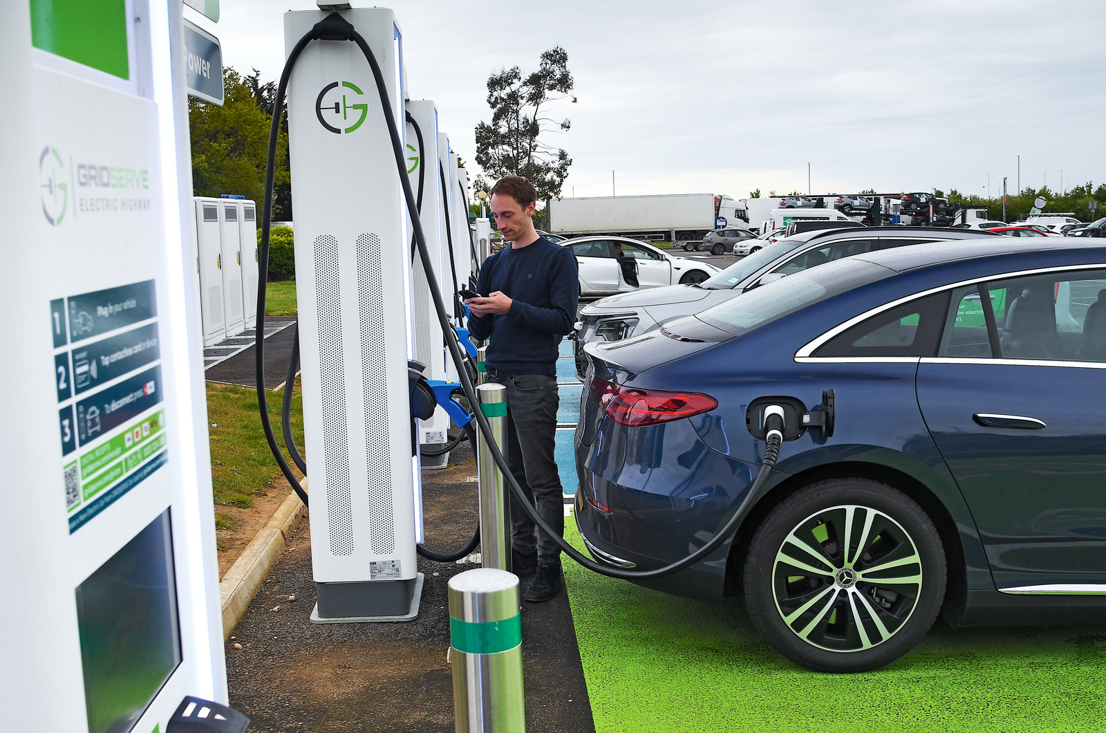 Person waiting for Mercedes EQE to charge at motorway services