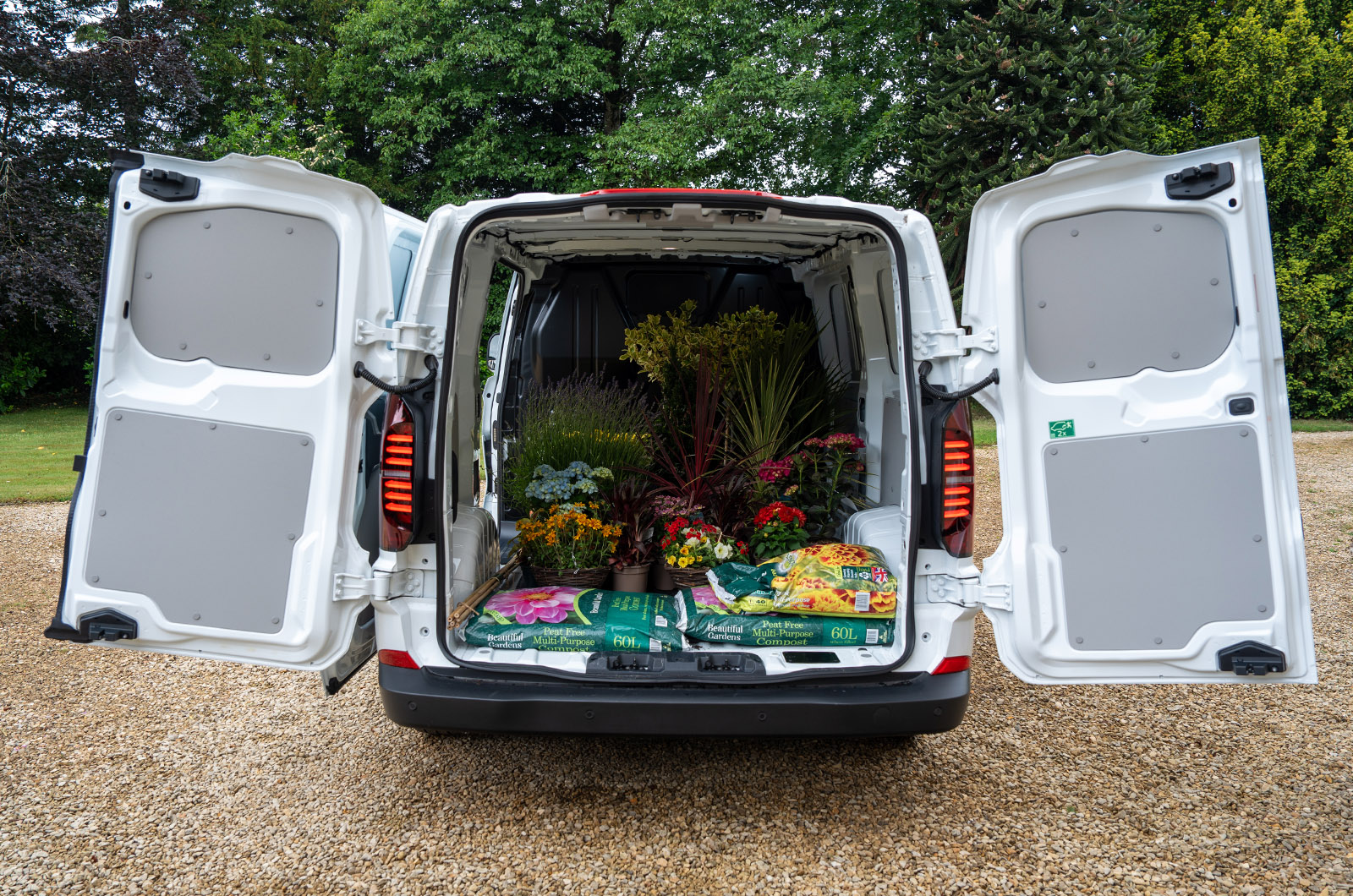 The cargo area of a white Volkswagen Transporter viewed through the rear doors. The load space is full of gardening materials.