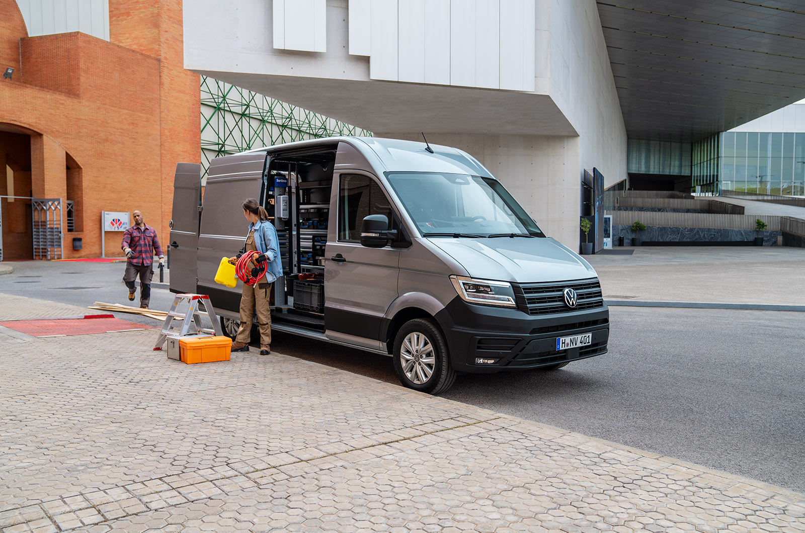 A silver Volkswagen Crafter parked at the roadside as two workers unload from a side door