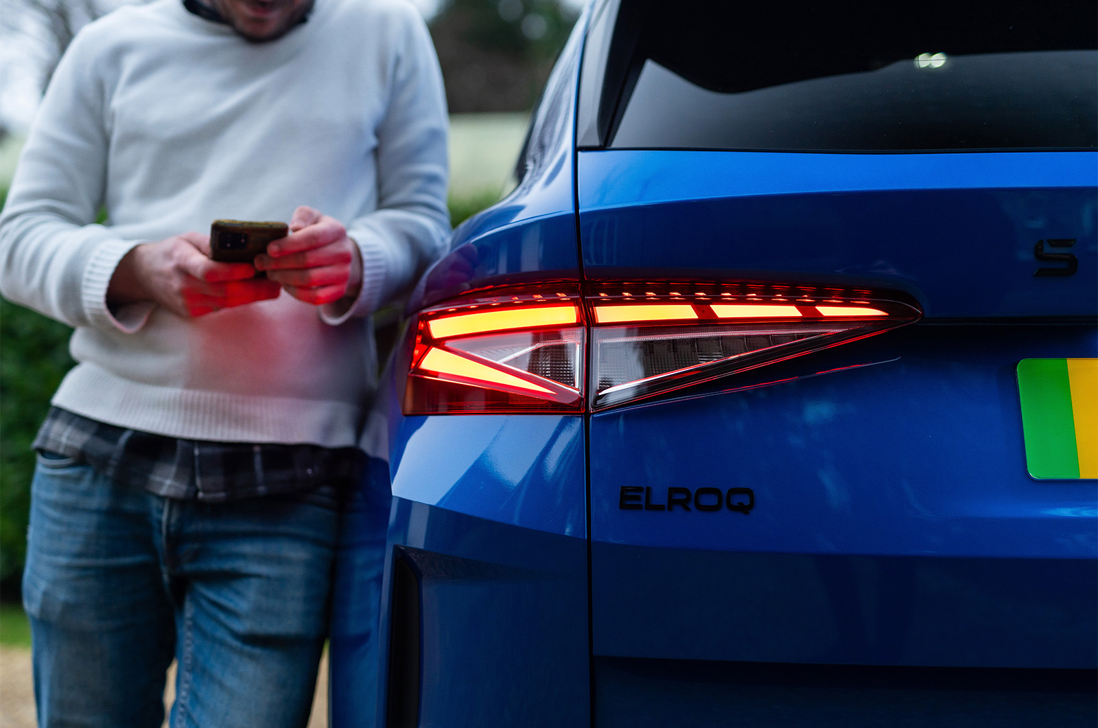 Man using Skoda App on phone next to rear of a blue Skoda Elroq