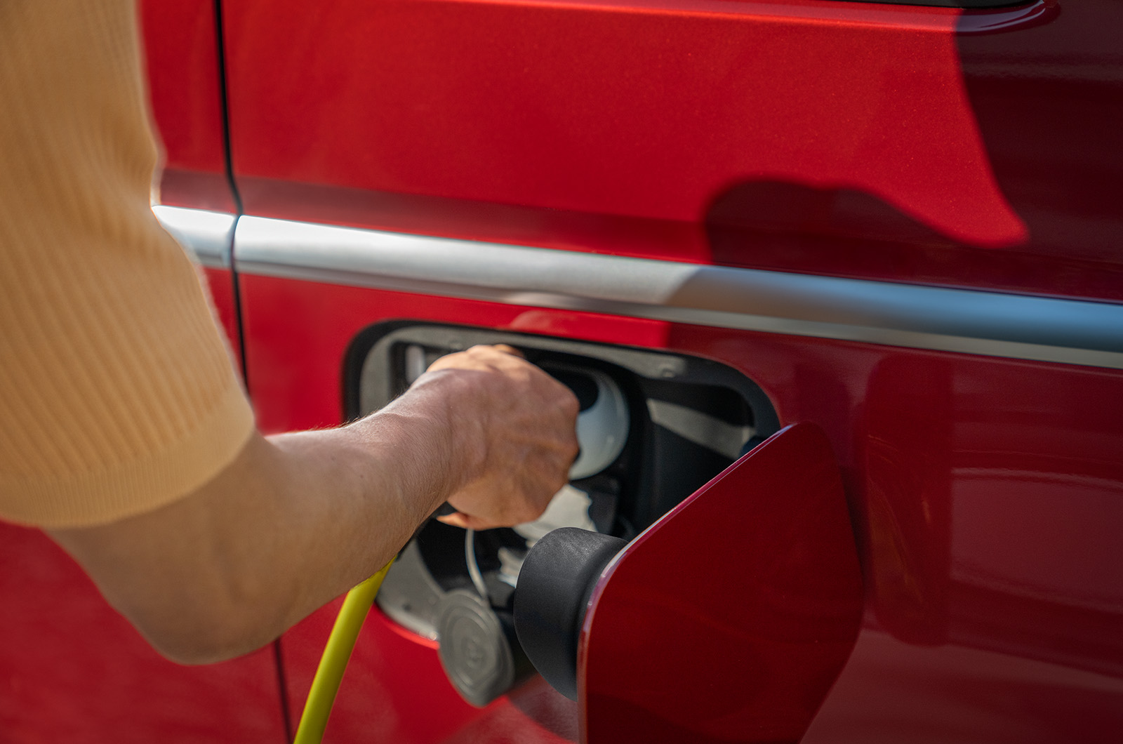 Hand putting a plug into a red Volkswagen Multivan ehybrid PHEV