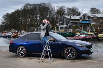 BMW i5 LT with person on ladder looking through binoculars