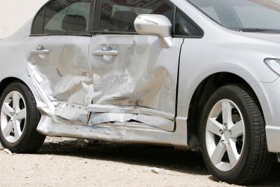 A silver coloured car with crash damage to the doors
