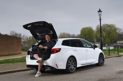 Jonty sitting in LT Toyota Corolla Touring Sports boot and holding a camera