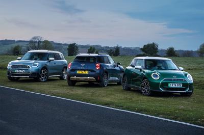 The all-electric Cooper, Aceman and Countryman parked together in front of a scenic countryside backdrop