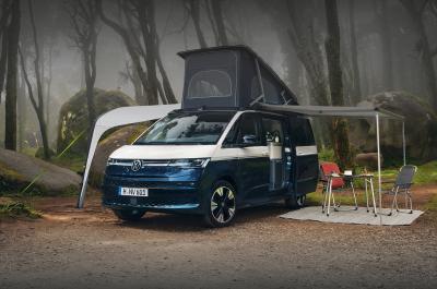 A blue and white Volkswagen California with twin awnings and a table and chairs set up