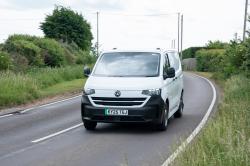 A white Volkswagen Transporter driving on a country road